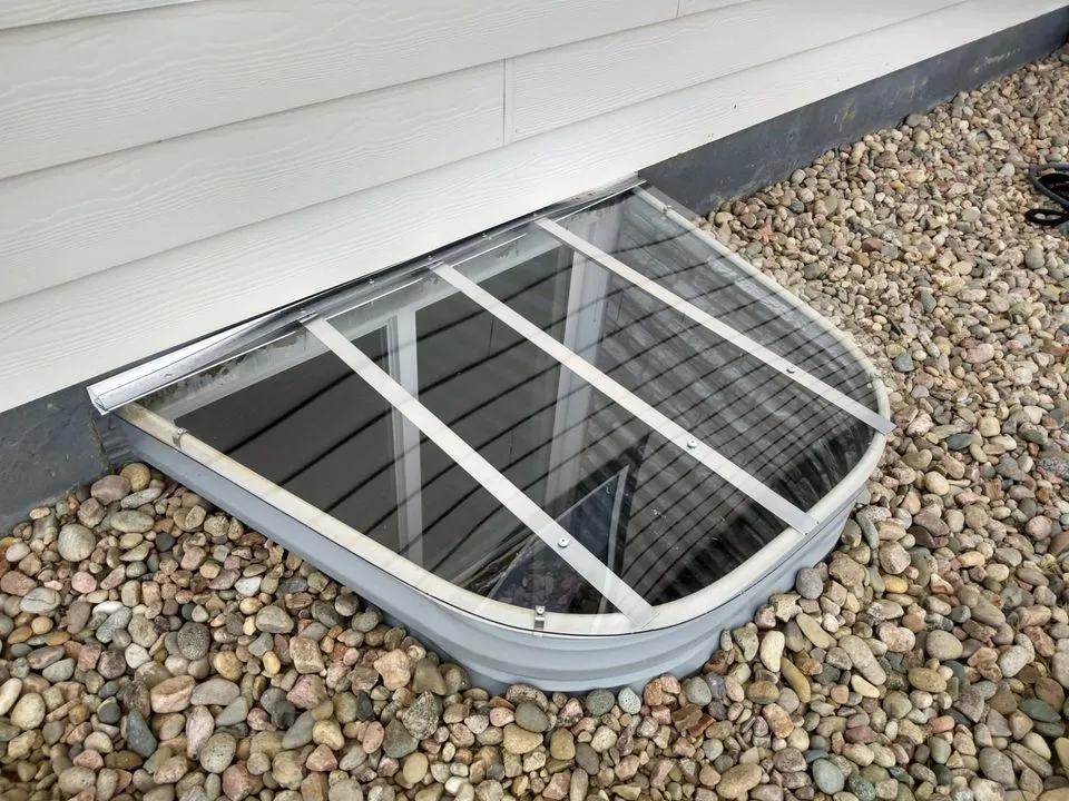 Clear polycarbonate window well cover installed on a basement window, designed for durability and protection.